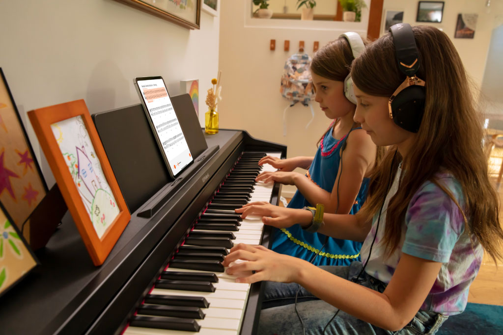 Two young children practicing the piano with headphones on